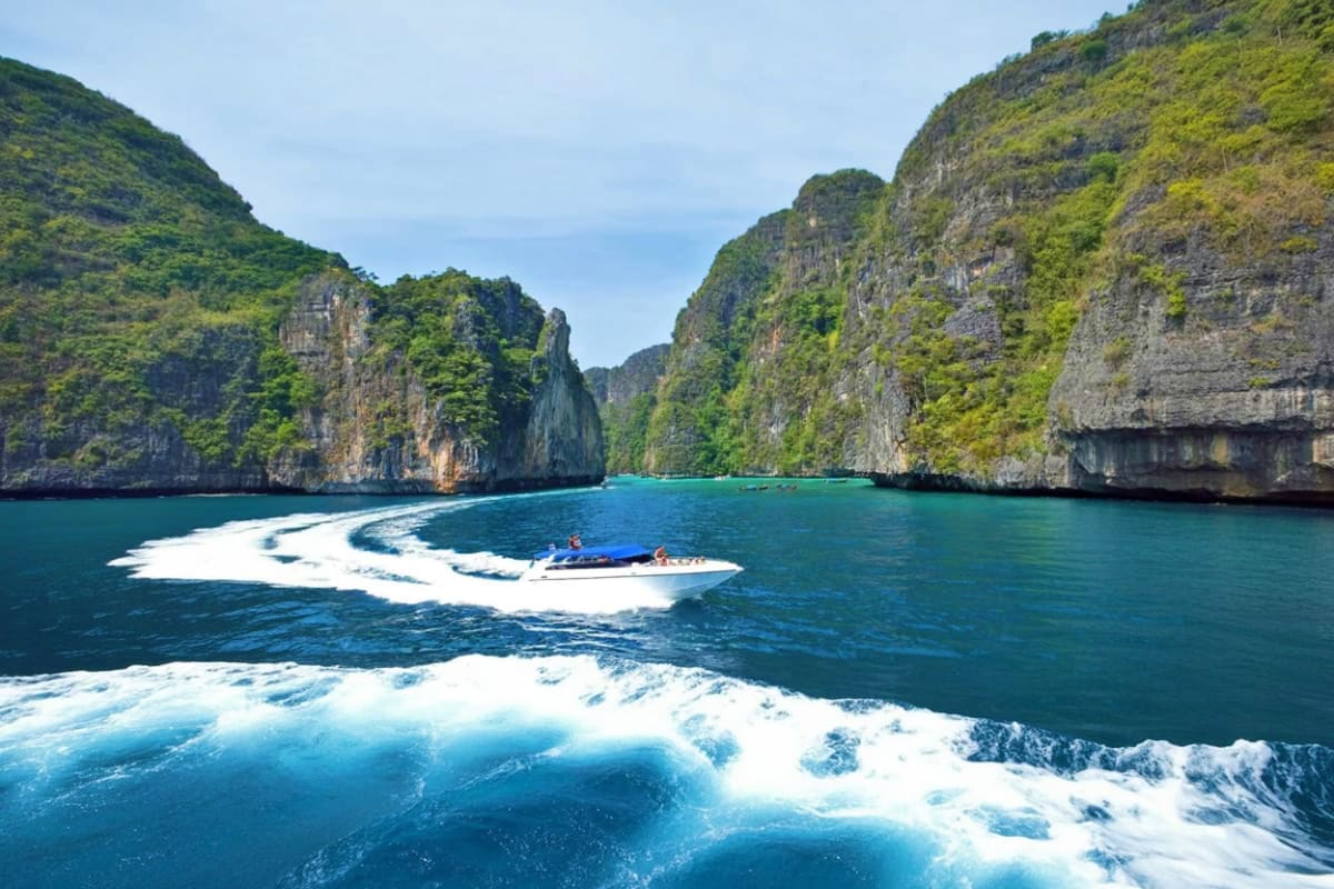 Hong Island Tour by Speed Boat Speedboat with tourists navigating turquoise waters between towering limestone cliffs in Hong Island, Thailand
