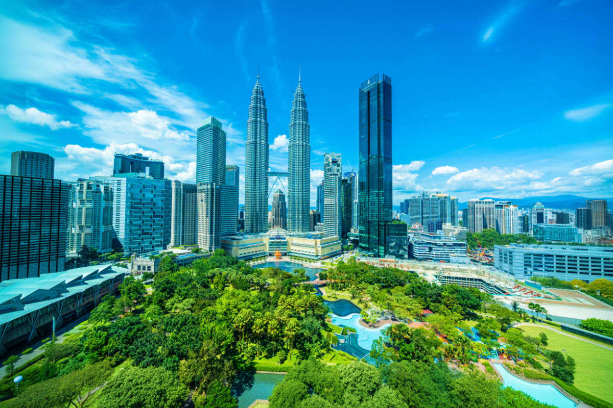 Aerial view of Kuala Lumpur skyline featuring iconic Petronas Twin Towers with surrounding park and modern buildings under bl