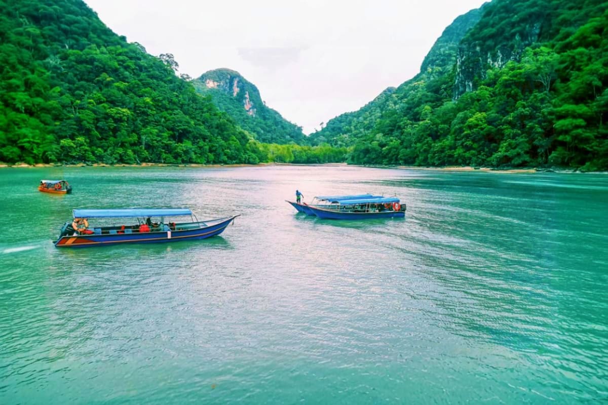 Traditional wooden fishing boats anchored in turquoise waters with limestone cliffs and dense jungle forest in Langkawi, Mala