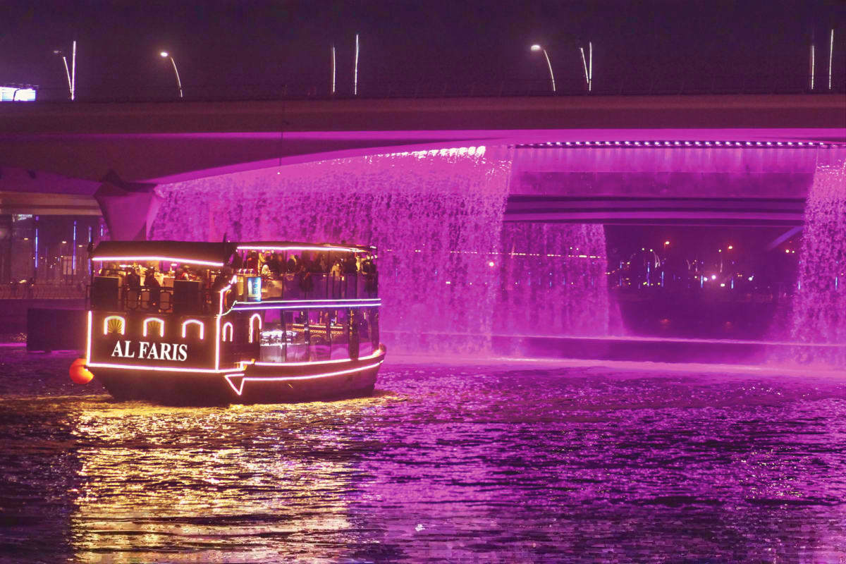 Al Faris luxury abra boat on Dubai Canal at night with illuminated purple bridge and waterfall fountain