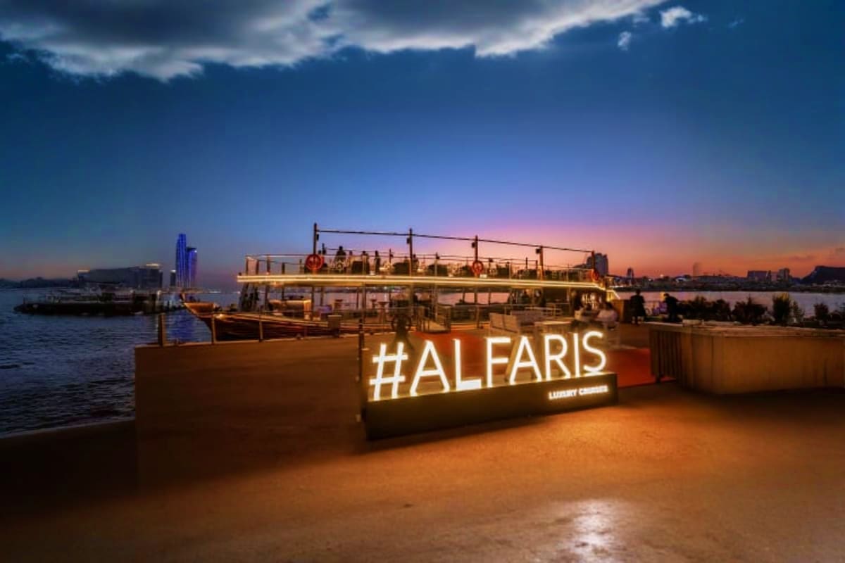 Al Faris luxury dinner cruise boat on Dubai Creek at sunset with illuminated sign and city skyline