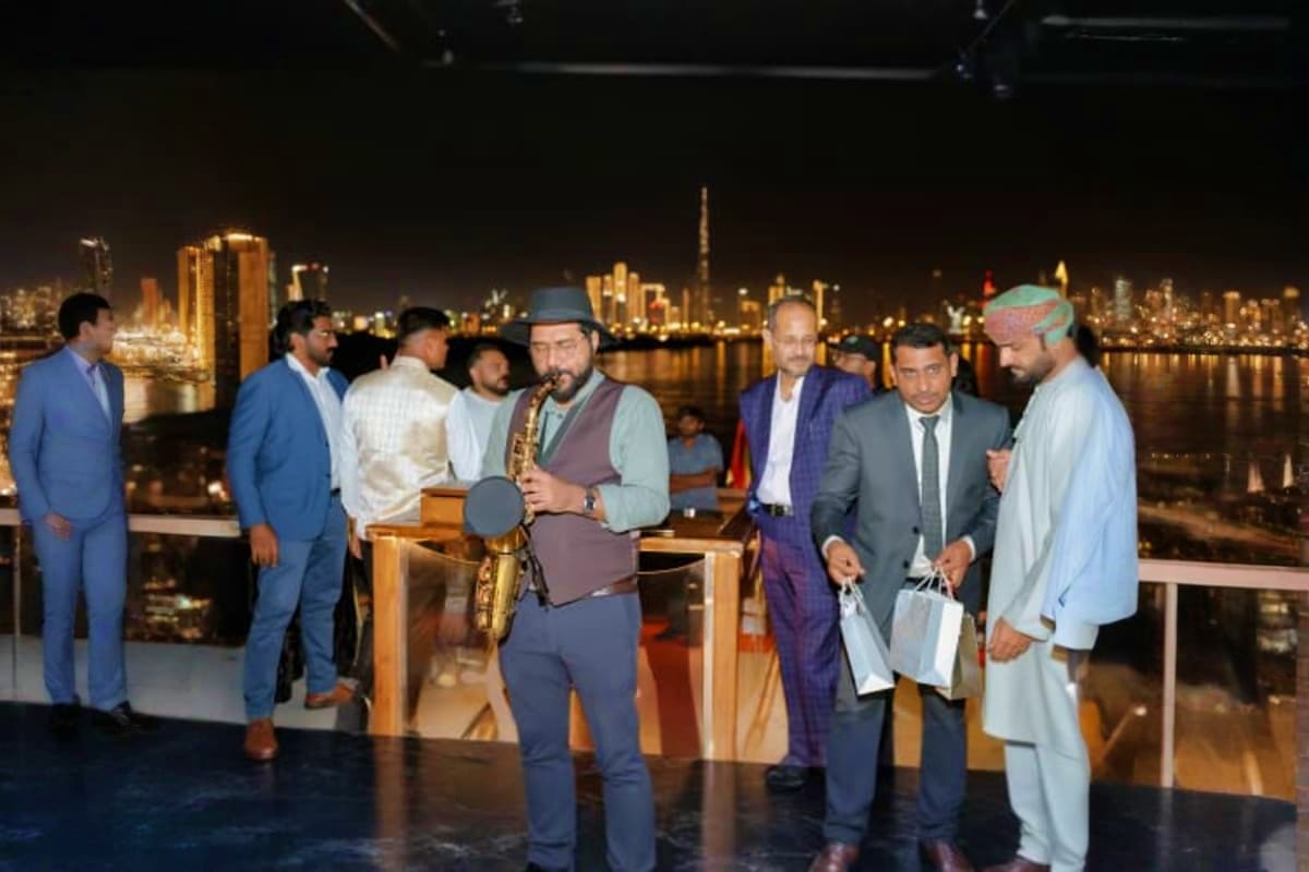 Group of men in formal and traditional Middle Eastern attire at nighttime event on luxury yacht with Dubai skyline and illumi
