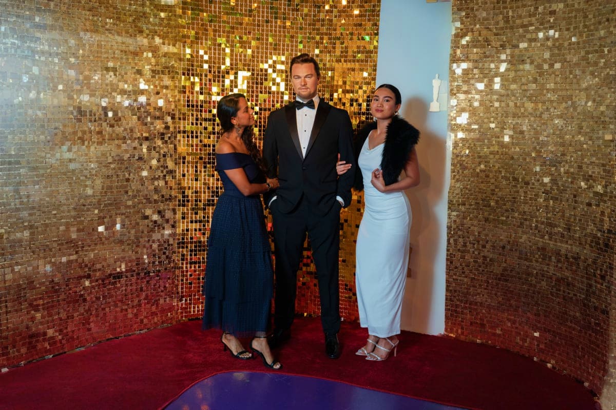 Madame Tussauds Dubai Three wax figures in formal attire posing together on a red carpet against a shimmering gold sequined backdrop at Madame Tuss