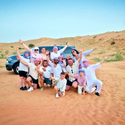 Mega Safari with Dinner In Ras Al Khaimah Large group of tourists posing together in desert sand with SUV vehicle and sand dunes in background during Ras Al Khaimah sa