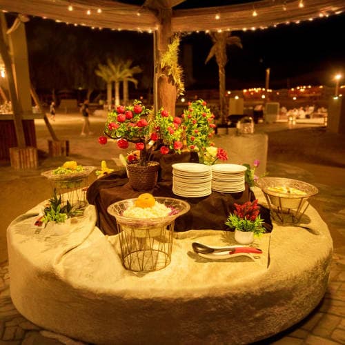 Outdoor dinner setup under string lights with floral centerpiece, table settings, and palm trees in desert landscape at night
