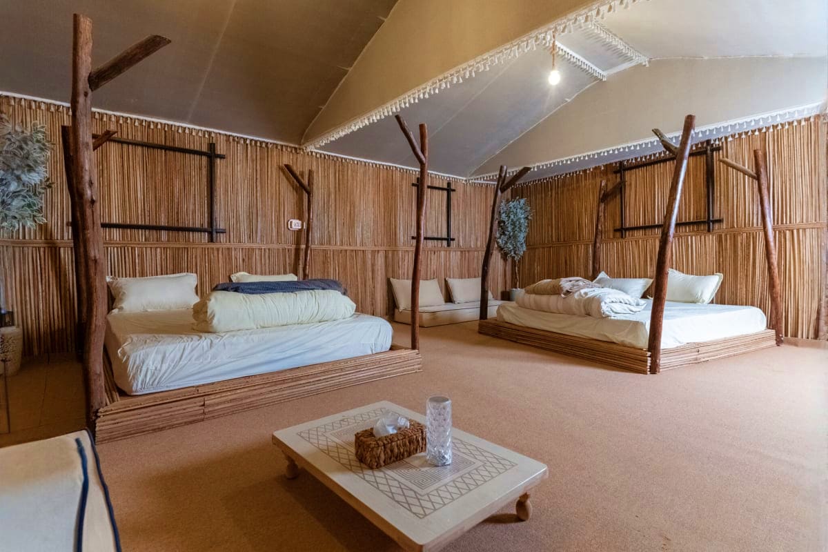 Spacious glamping room with rustic wooden four-poster beds, corrugated metal walls, and desert safari accommodation interior