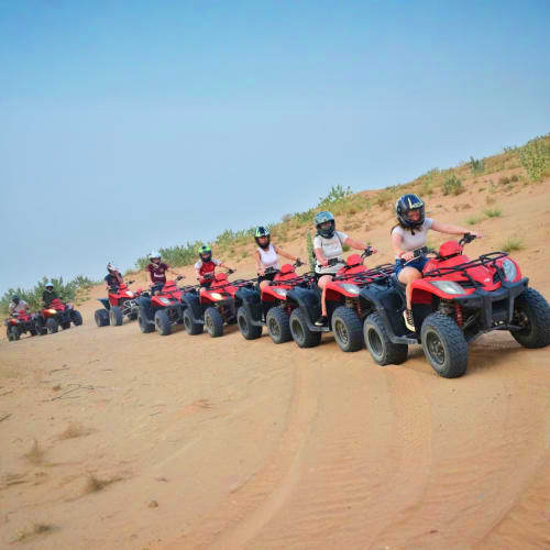 Group of riders on red quad bikes lined up on sandy desert terrain with sparse vegetation and clear blue sky in Ras Al Khaima