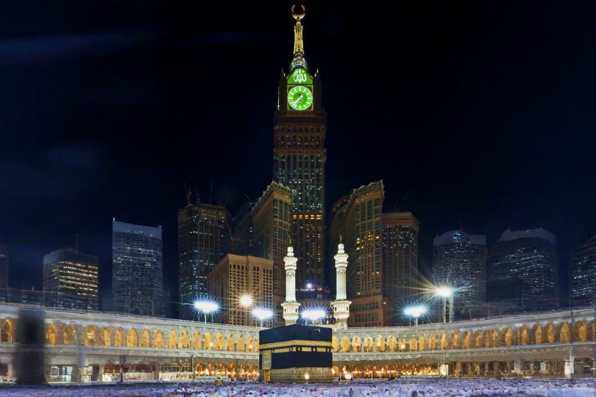 Illuminated Kaaba and Grand Mosque courtyard at night in Makkah with surrounding arcades and cityscape