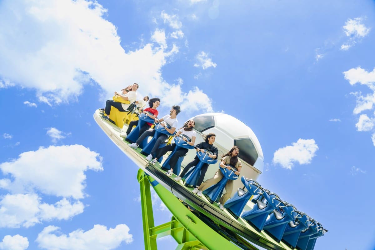 Roller coaster at Real Madrid World Dubai with passengers on bright green and yellow track against blue sky with clouds