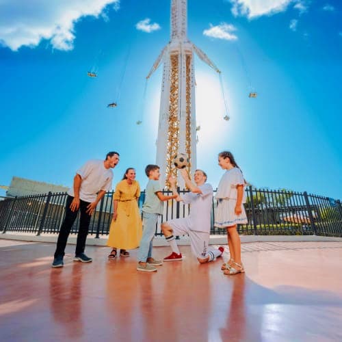 Family standing together at Real Madrid World Dubai entrance with tall white tower structure and blue sky in background
