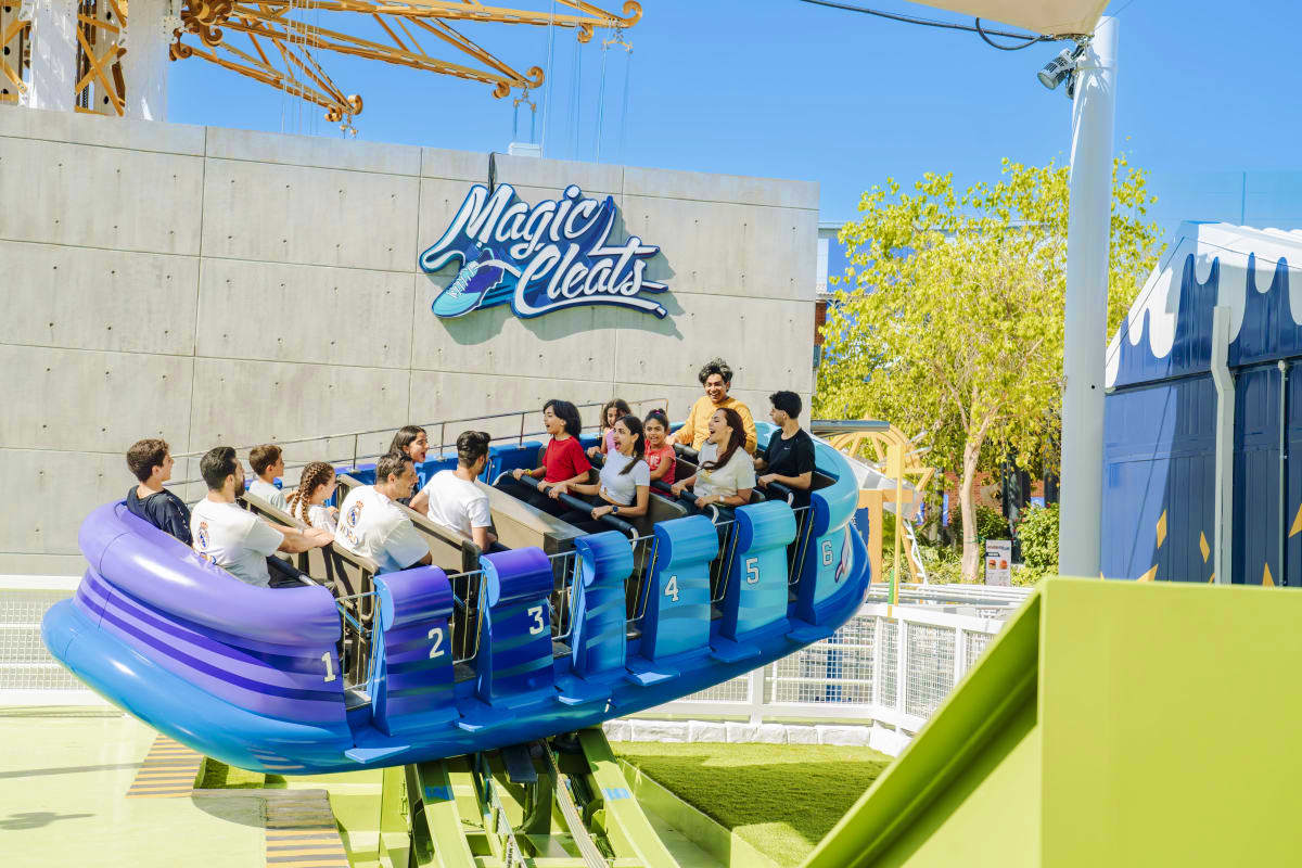 Guests riding the blue Magic Pleats roller coaster at Real Madrid World Dubai theme park under clear blue sky