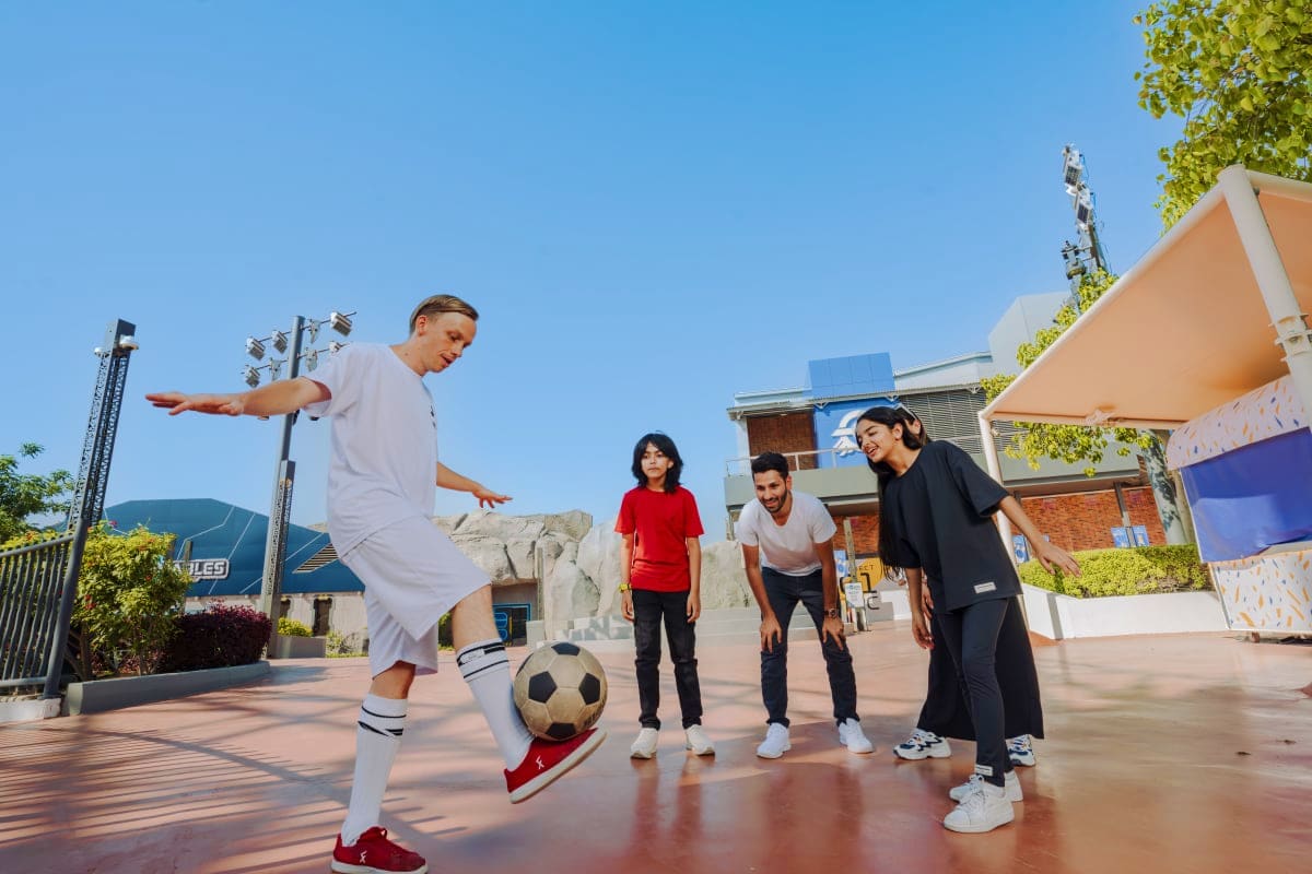 Man kicking soccer ball while group of children watch in outdoor plaza at Real Madrid World Dubai attraction