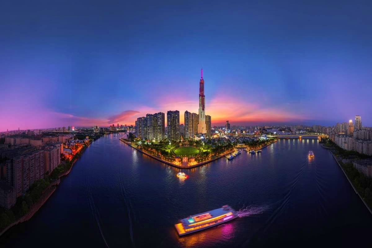 Aerial view of Bitexco Financial Tower at sunset with illuminated skyscraper rising above Saigon River and cityscape, colorfu