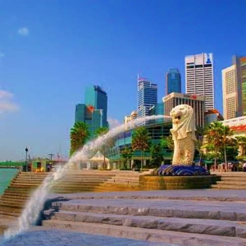 Merlion statue spouting water with Singapore skyline and modern skyscrapers in background under clear blue sky