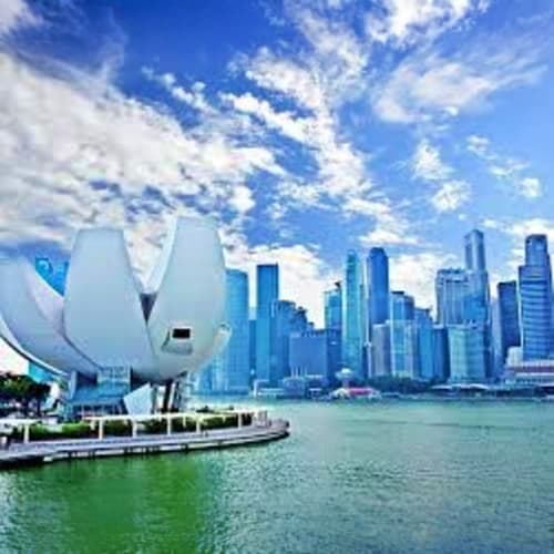 Guided Singapore Layover City Tour Modern white sail-shaped building on waterfront with Chicago skyline and skyscrapers reflected in blue-green water under clou