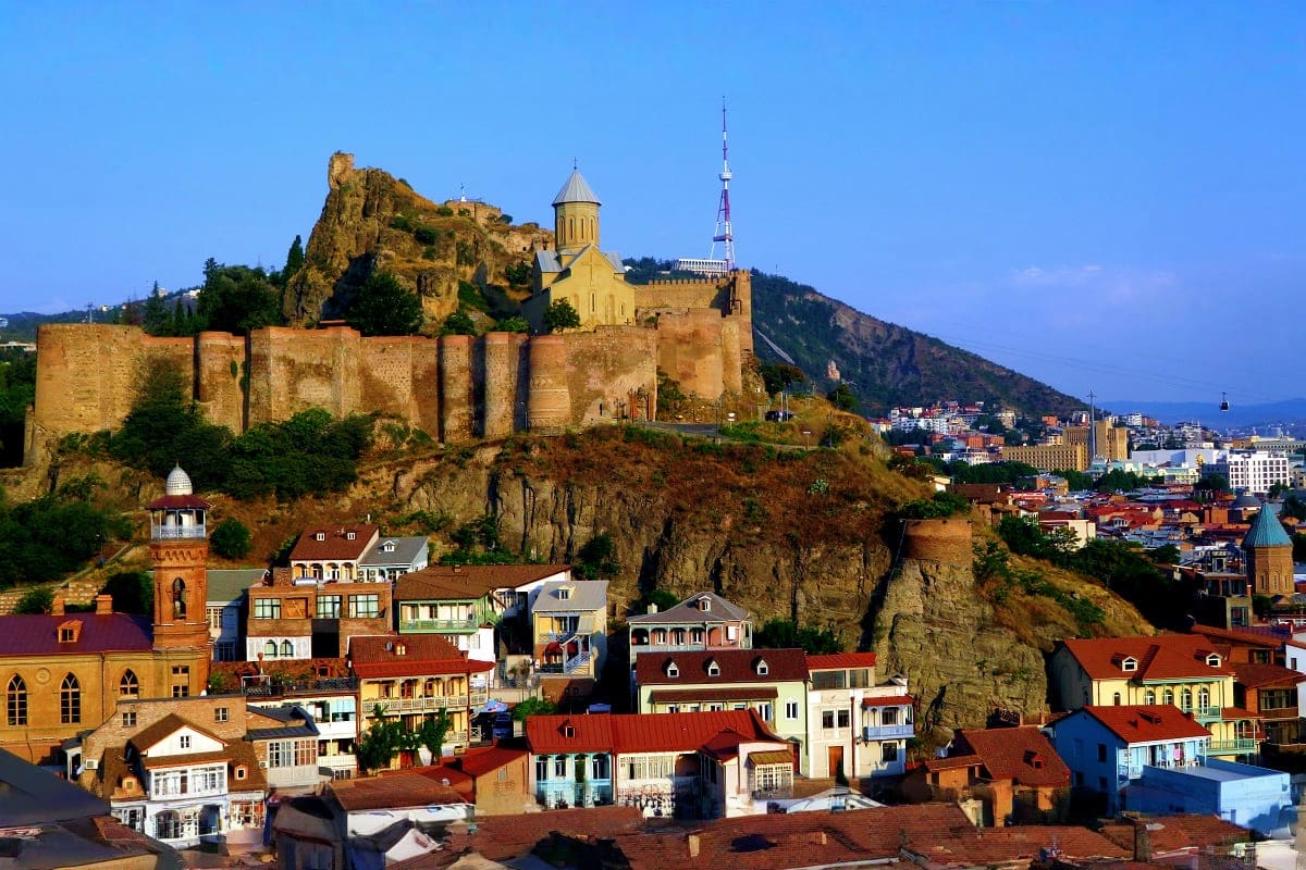 Metekhi Church and fortress overlooking colorful historic buildings in Tbilisi with clear blue sky