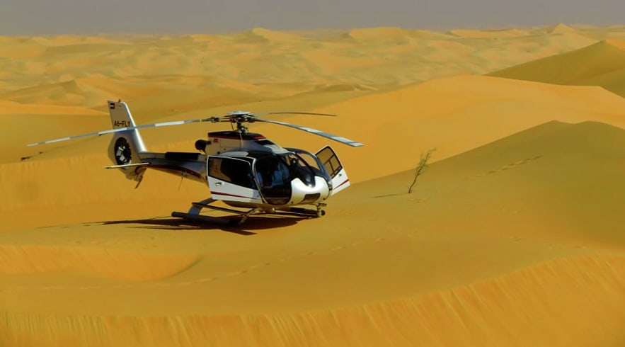 Private Helicopter Tour in Dubai White and black helicopter landed on sand dunes in Dubai desert landscape