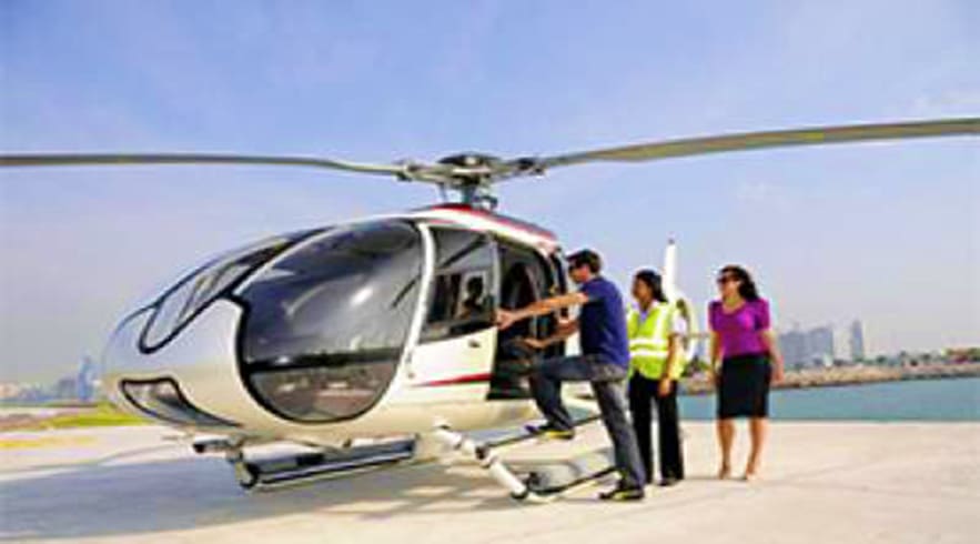 Passengers boarding a white helicopter on a helipad with Dubai skyline and waterfront in the background