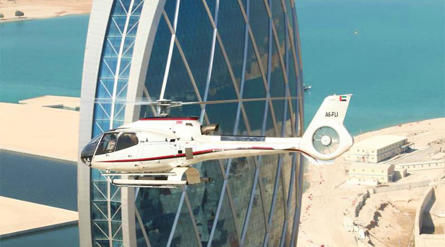 Helicopter flying past Burj Al Arab with Dubai coastline and turquoise water visible below