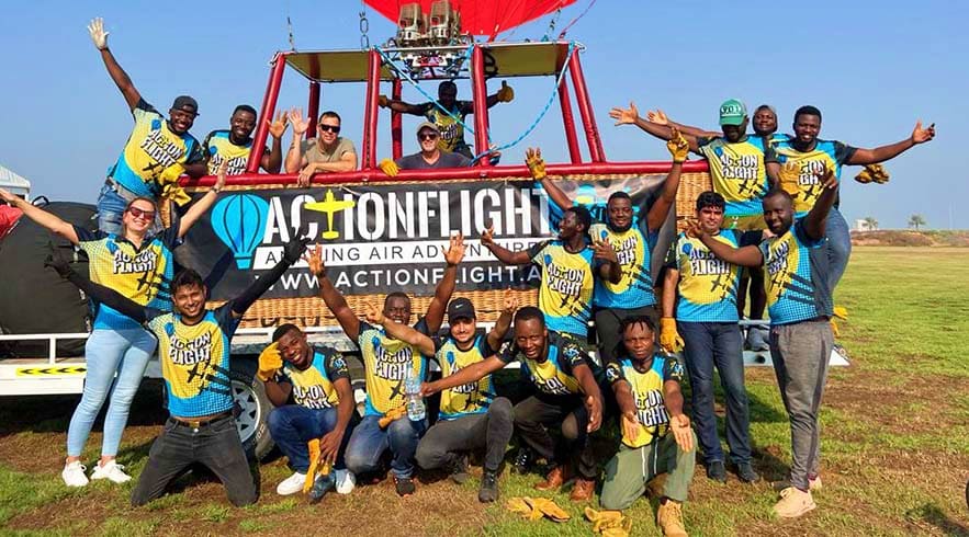 Sunrise Hot Air Balloon Ras Al Khaimah Group of people wearing yellow and blue shirts posing in front of a red hot air balloon basket and ActionFlight signage in an