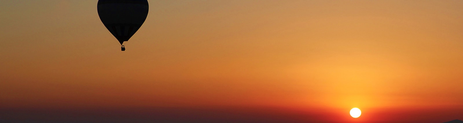 Black hot air balloon silhouetted against golden sunrise sky over desert landscape in Ras Al Khaimah
