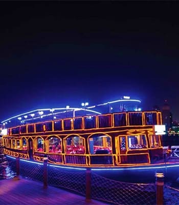 Illuminated traditional dhow boat with golden ornate details docked at marina at night, ready for dinner cruise