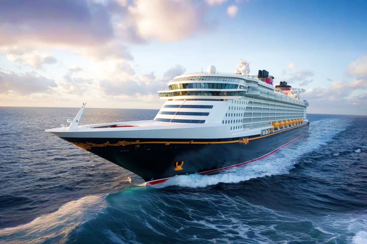 Large white and black cruise ship with yellow lifeboats sailing through blue ocean waters under partly cloudy sky