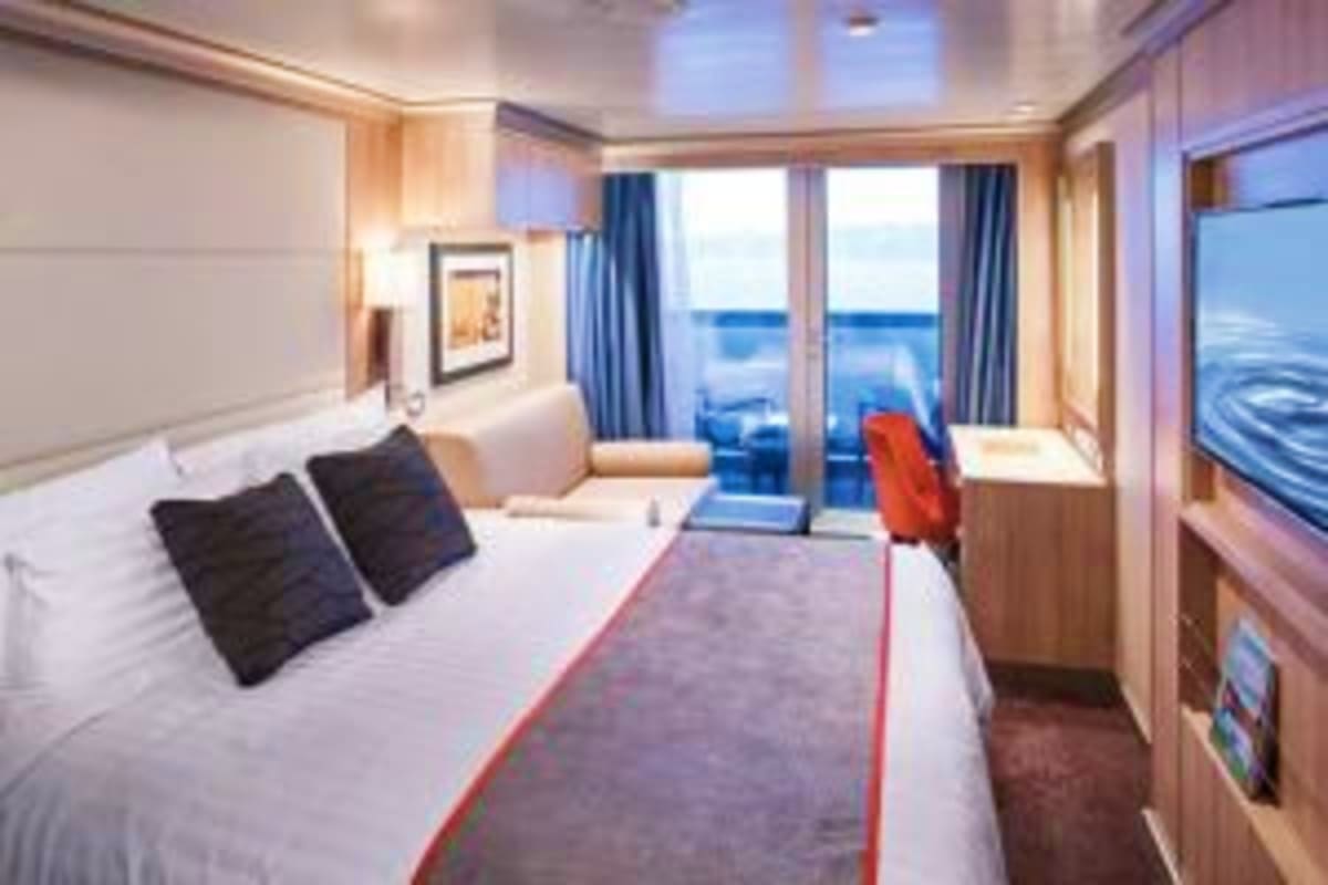 Luxury cruise ship stateroom with queen bed, ocean view balcony, and modern furnishings overlooking the sea