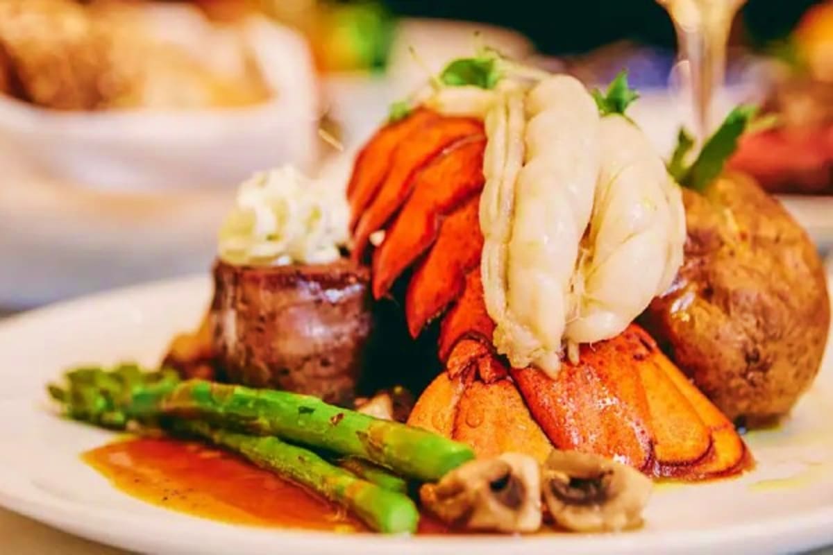 Gourmet lobster tail dinner plated with asparagus, roasted vegetables, and garnish on fine dining cruise ship restaurant tabl