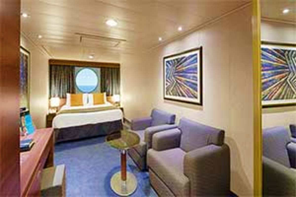 Luxury cruise ship stateroom with bed, seating area, porthole window, and modern decor on MSC Preziosa