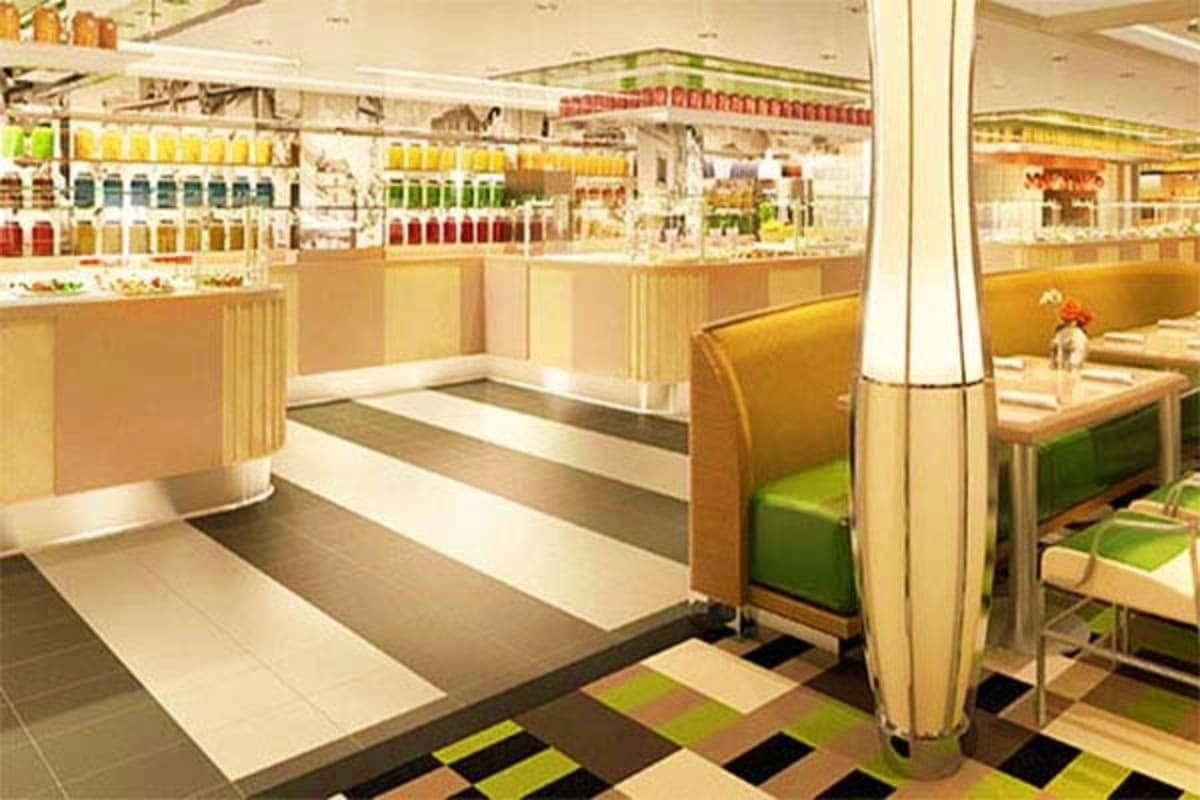 Modern juice bar interior with colorful bottles on shelves, beige and green seating booths, and geometric floor tiles on Nieu