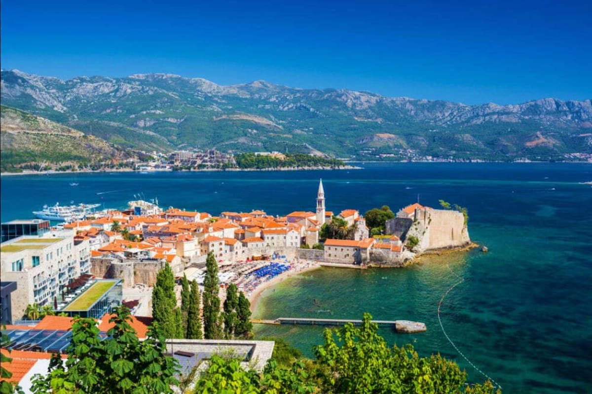 Budva old town coastal cityscape with terracotta roofs, fortified walls, bell tower, and turquoise Adriatic Sea with mountain