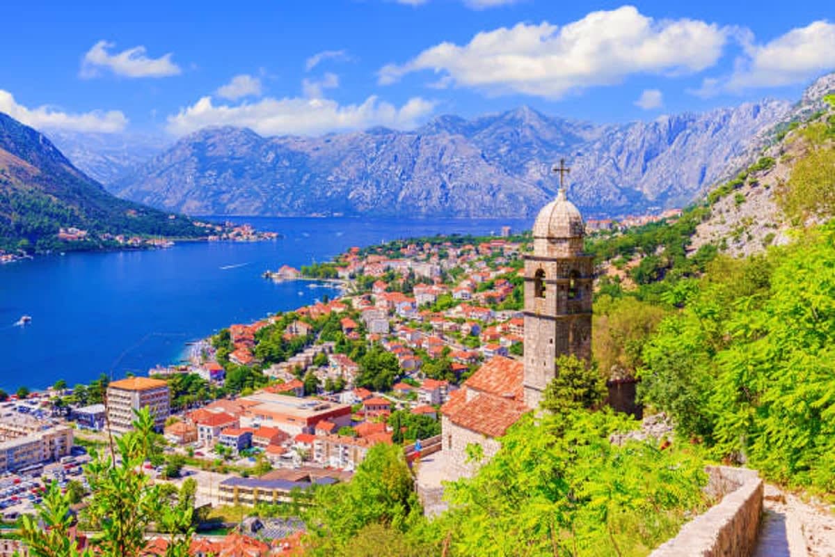Kotor Bay coastal town with stone church bell tower, red-roofed houses, mountains and blue Adriatic Sea water in Montenegro