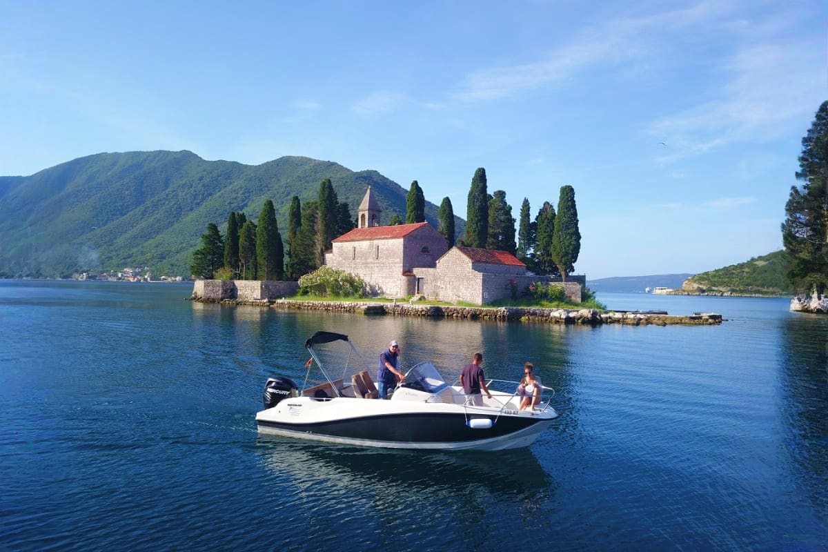 Speedboat with tourists near Church of Our Lady of the Rocks on Lake Kotor, Montenegro surrounded by cypress trees and mounta