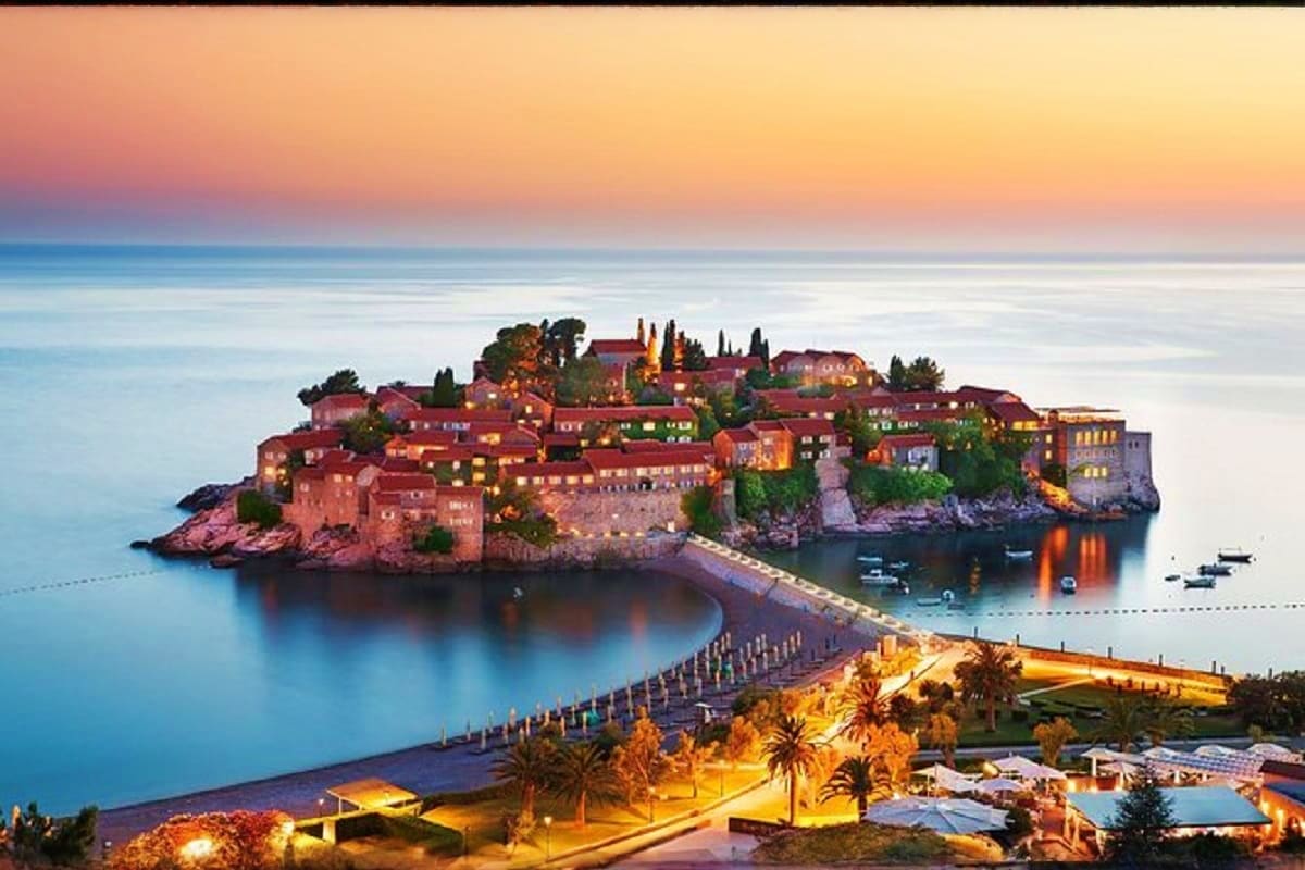 Sveti Stefan island at sunset with illuminated medieval village, causeway, and Adriatic Sea in Montenegro