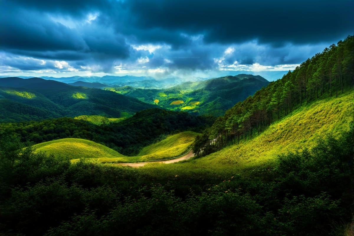 Lush green mountain valley with winding dirt road, dense forests, and layered peaks under dramatic cloudy sky