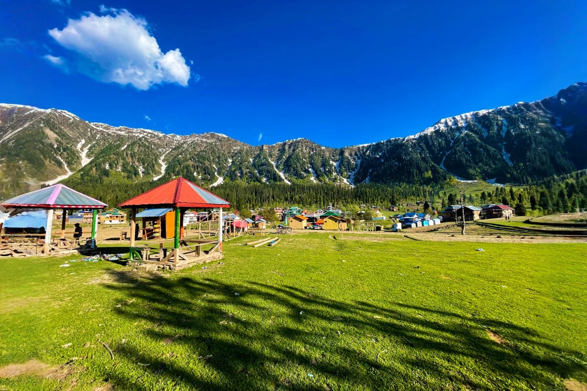 Alpine valley settlement with colorful wooden structures and red umbrellas beneath snow-capped mountains in Uzbekistan