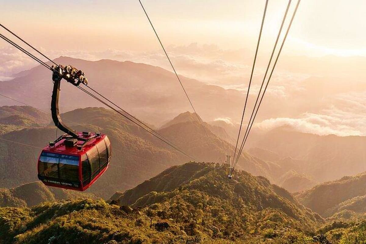 Red cable car suspended above lush forested mountains at sunset in Vietnam
