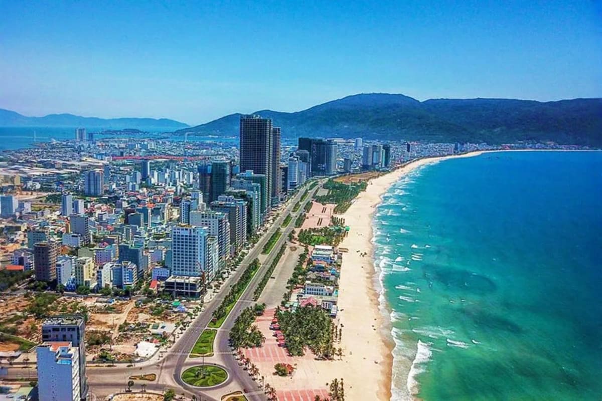 Aerial view of Benidorm beachfront with sandy shore, turquoise water, high-rise hotels and mountains under clear blue sky