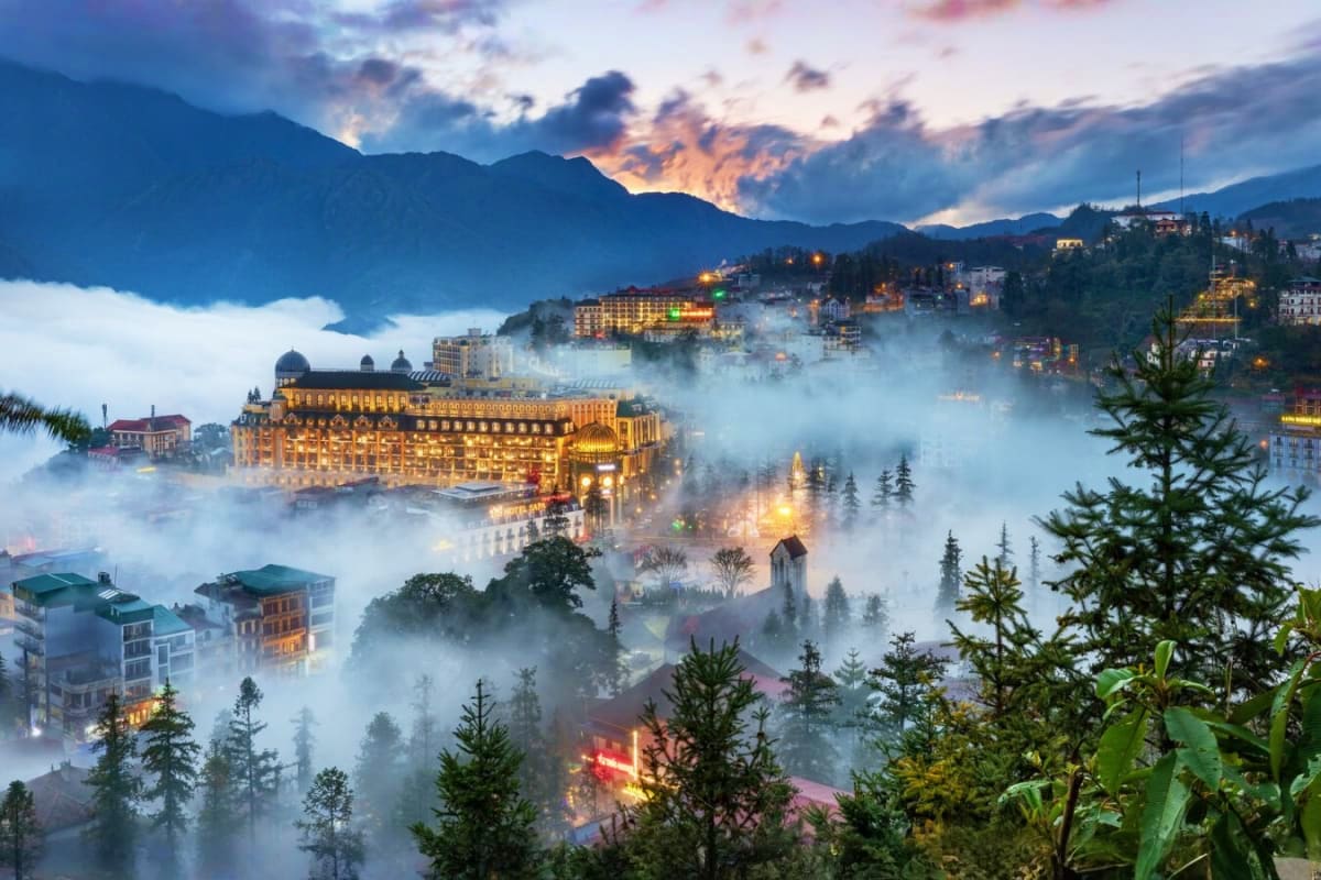 Illuminated luxury resort nestled in misty mountain valley at dusk in Sapa, Vietnam, with forest and distant peaks