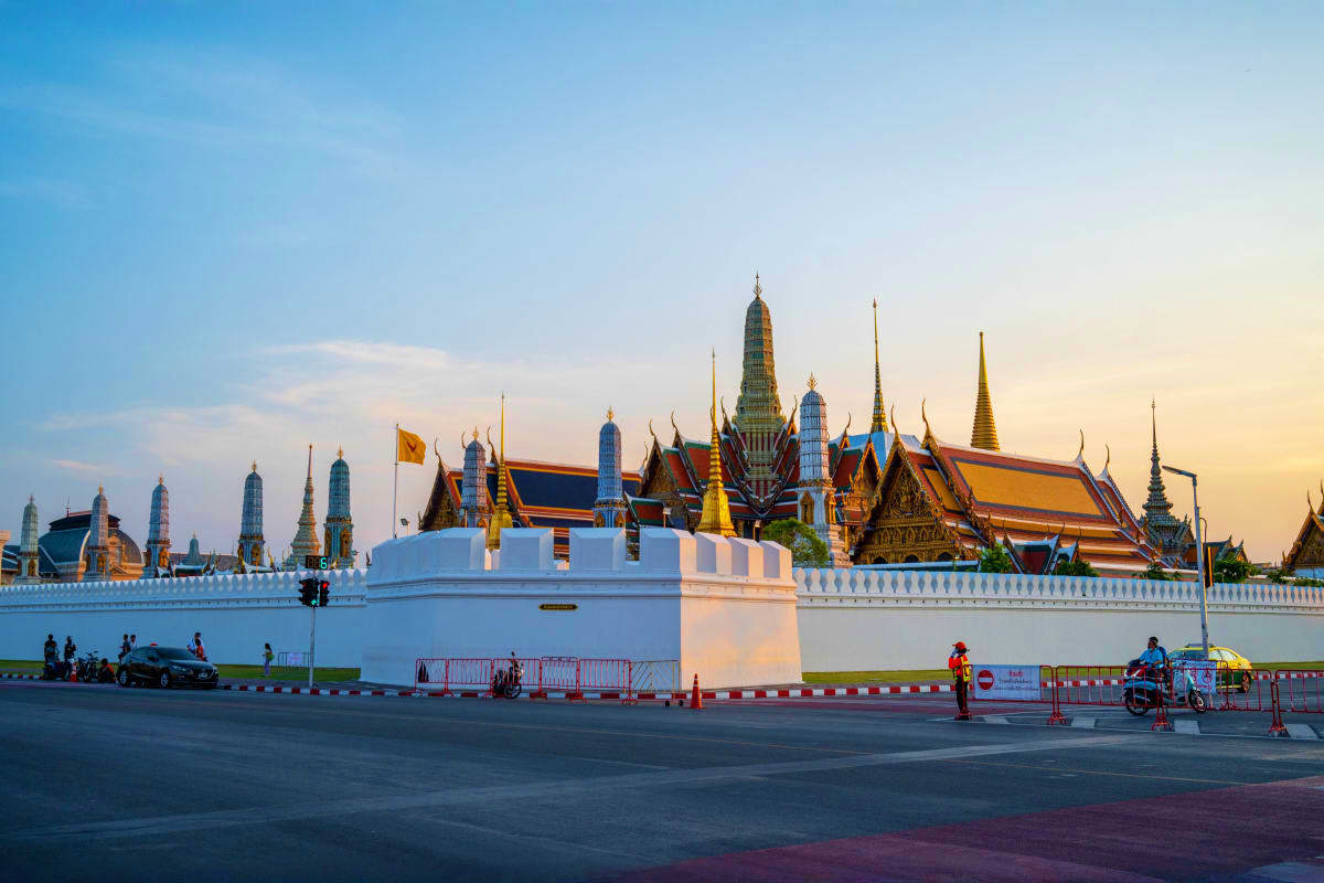 Grand Palace in Bangkok Thailand with golden spires and white walls at sunset, iconic Buddhist temple complex landmark
