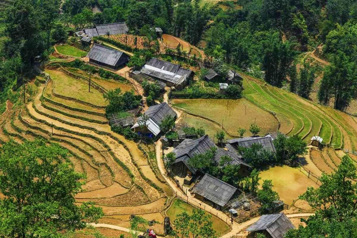 Aerial view of traditional Vietnamese village with terraced rice paddies, wooden houses with dark roofs, and flooded fields s