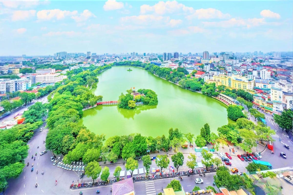 Aerial view of Hoan Kiem Lake in Hanoi, Vietnam, surrounded by lush green trees and dense urban cityscape with buildings and 