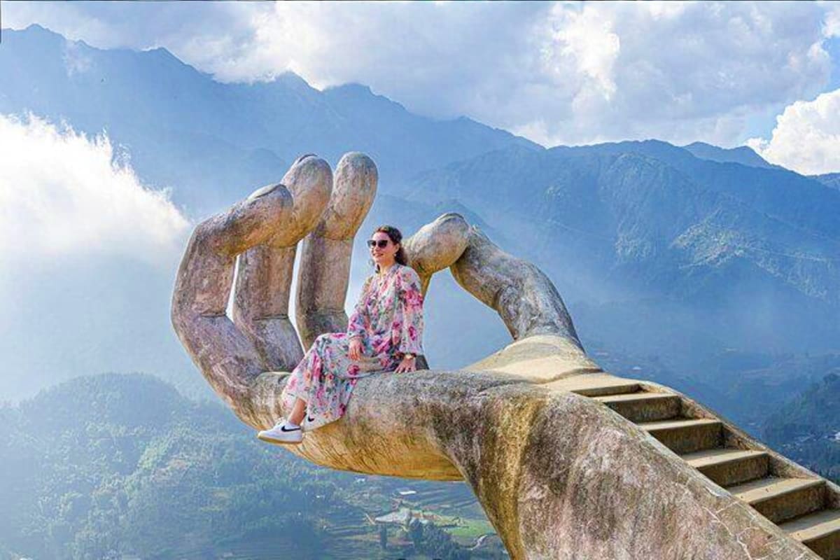 Woman sitting on giant stone hand sculpture overlooking mountainous valley landscape in Vietnam