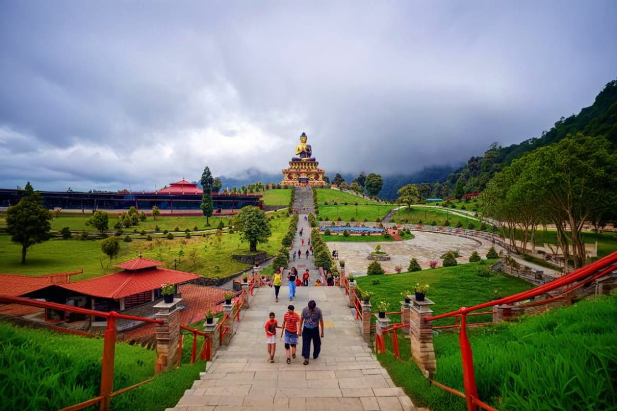 Pathway leading to golden Buddha statue at Namchi monastery in Sikkim with lush green grounds and mountain backdrop