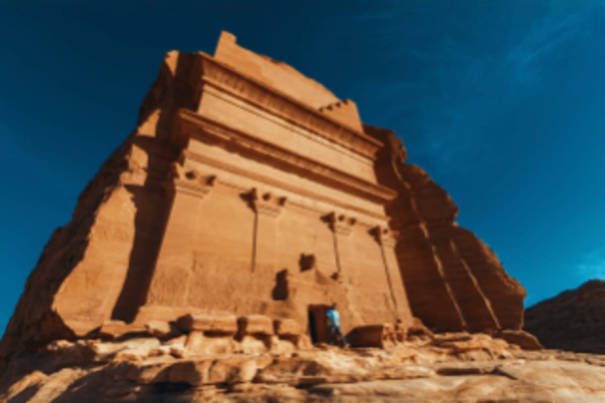 Ancient carved sandstone tomb structure against blue sky in desert landscape, Saudi Arabia historical monument