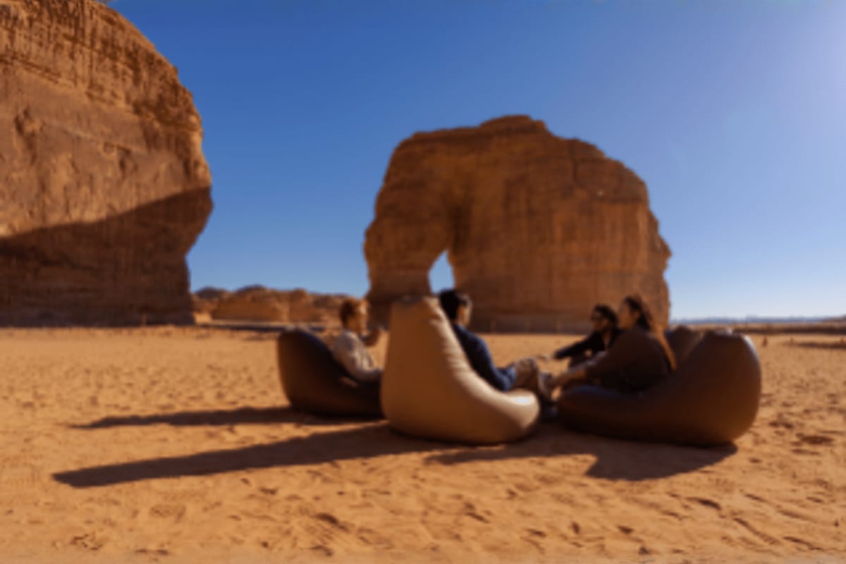 Tourists sitting in white bean bag chairs beneath the natural rock arch of Al-Rajajil in Saudi Arabian desert landscape
