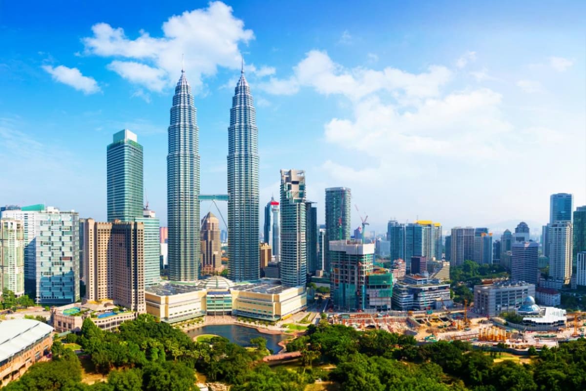 Singapore Malaysia Family tour Kuala Lumpur skyline featuring the iconic Petronas Twin Towers and surrounding city buildings under blue sky with clouds