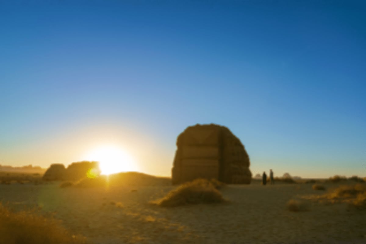 Sunset view of massive rock formation in desert landscape with visitors walking, clear blue sky