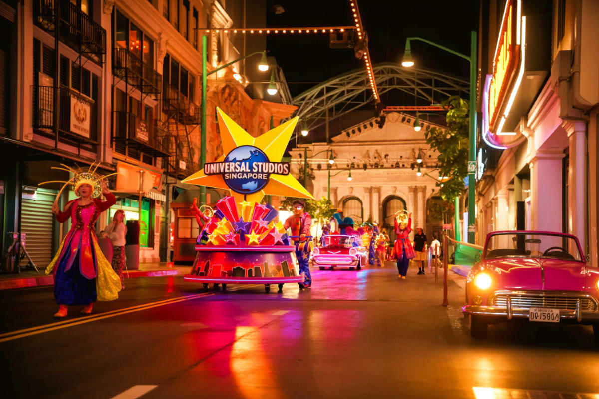 Exclusive Singapore and sentosa tour Universal Studios Singapore nighttime parade with illuminated floats, performers in costumes, vintage car, and colonial build